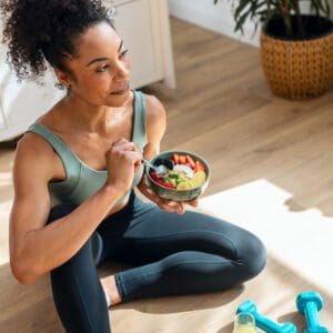 A woman sitting on the ground holding a bowl of fruit.