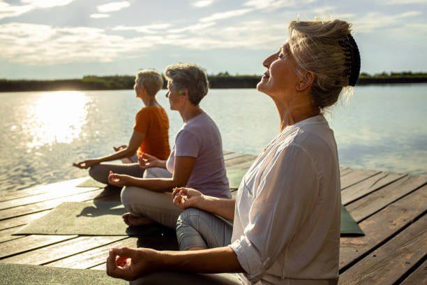 Women meditating on dock by water.