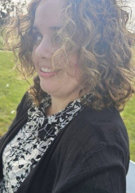 Woman with curly hair sitting outside smiling.
