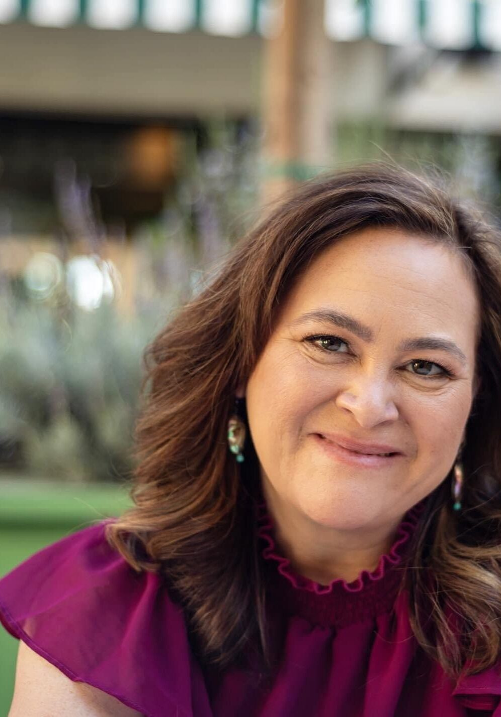 Smiling woman in a purple blouse outdoors.
