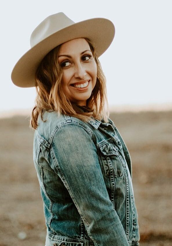 Smiling woman in hat and denim jacket.